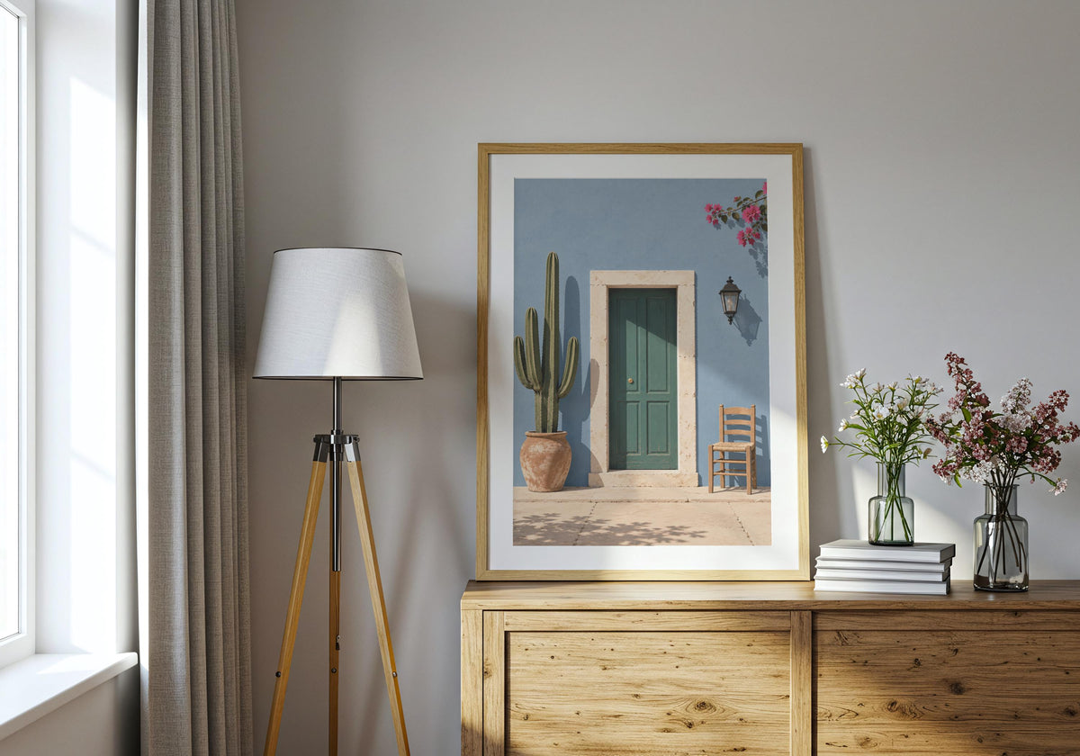 Blue Wall Green Door presented as blue wall art, featuring a forest-green door in a powder-blue wall with cactus, chair and flowers and displayed in a light wood frame on a bright console.