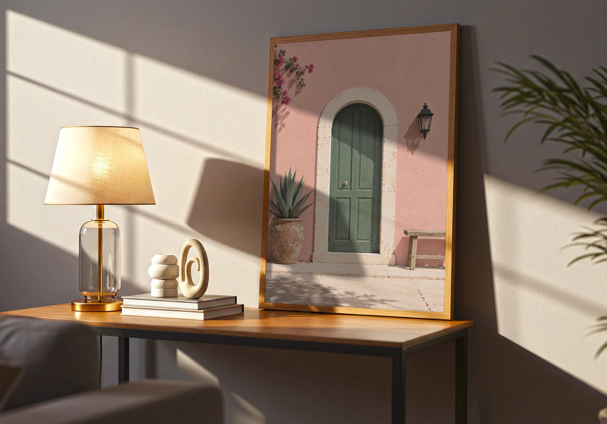 Wide interior view of summer wall print with an arched green door in a blush-pink wall with bougainvillea and a wooden bench, standing in a dark wood frame on a side table.