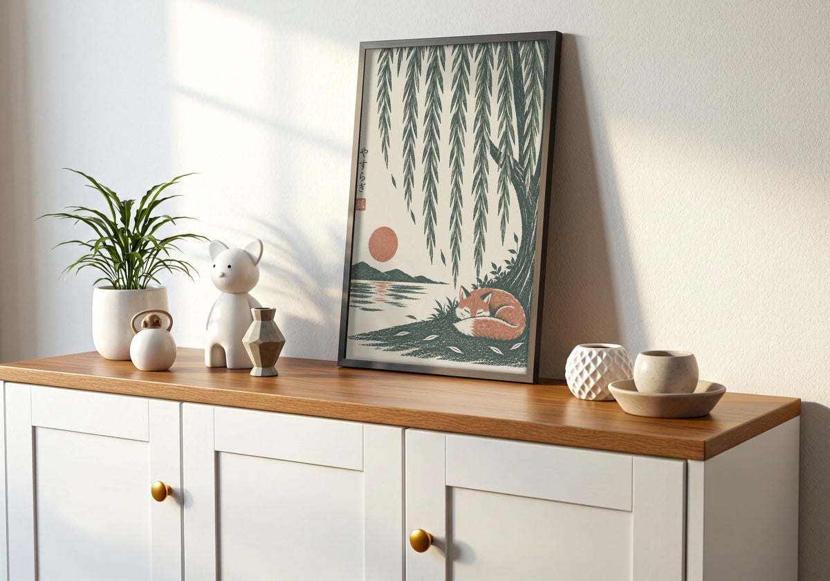 Interior mockup of willow tree print depicting a rust-coloured fox curled asleep beneath cascading willow branches and a low sun, displayed in a black frame on a wooden console.