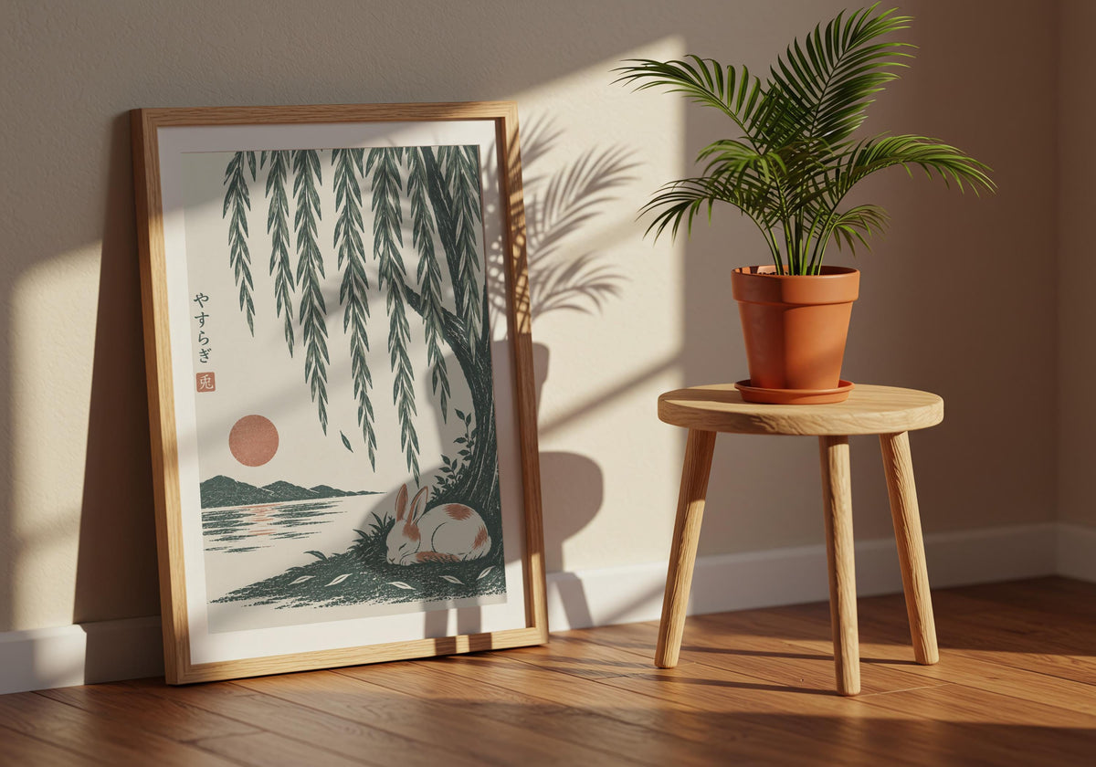 Angled view of nature wall poster depicting a small white rabbit sleeping beside green water beneath long willow leaves, leaning in a dark wood frame beside a terracotta plant.