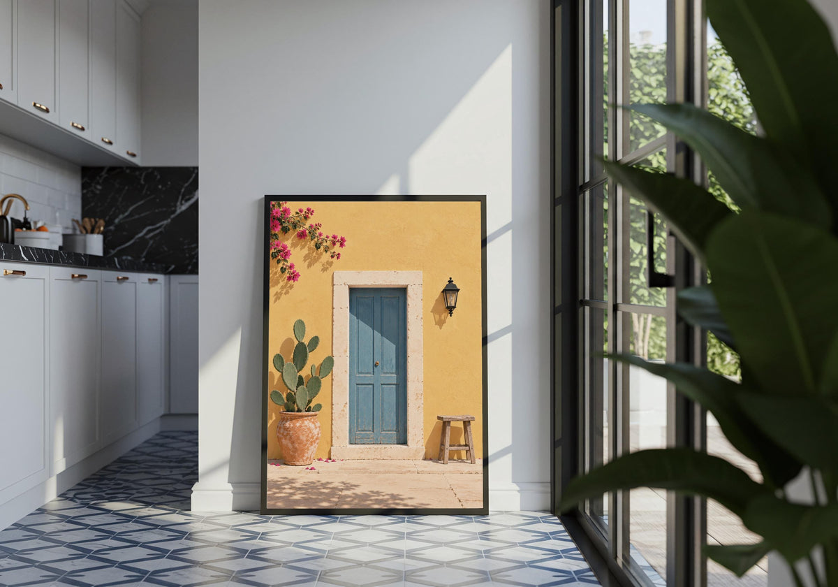 Portrait entryway wall art featuring a dusty-blue door in a sunny yellow wall with cactus, stool and bougainvillea, displayed in a black frame in a tiled interior.