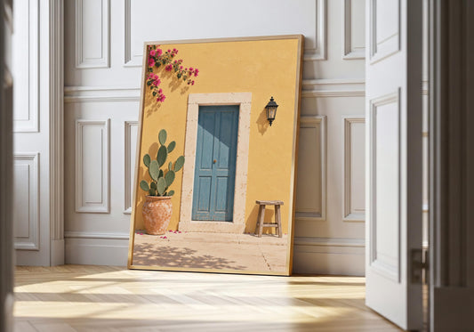 Blue door print showing a dusty-blue door in a sunny yellow wall with cactus, stool and bougainvillea, leaning in a light natural-wood hero frame against white panelling.