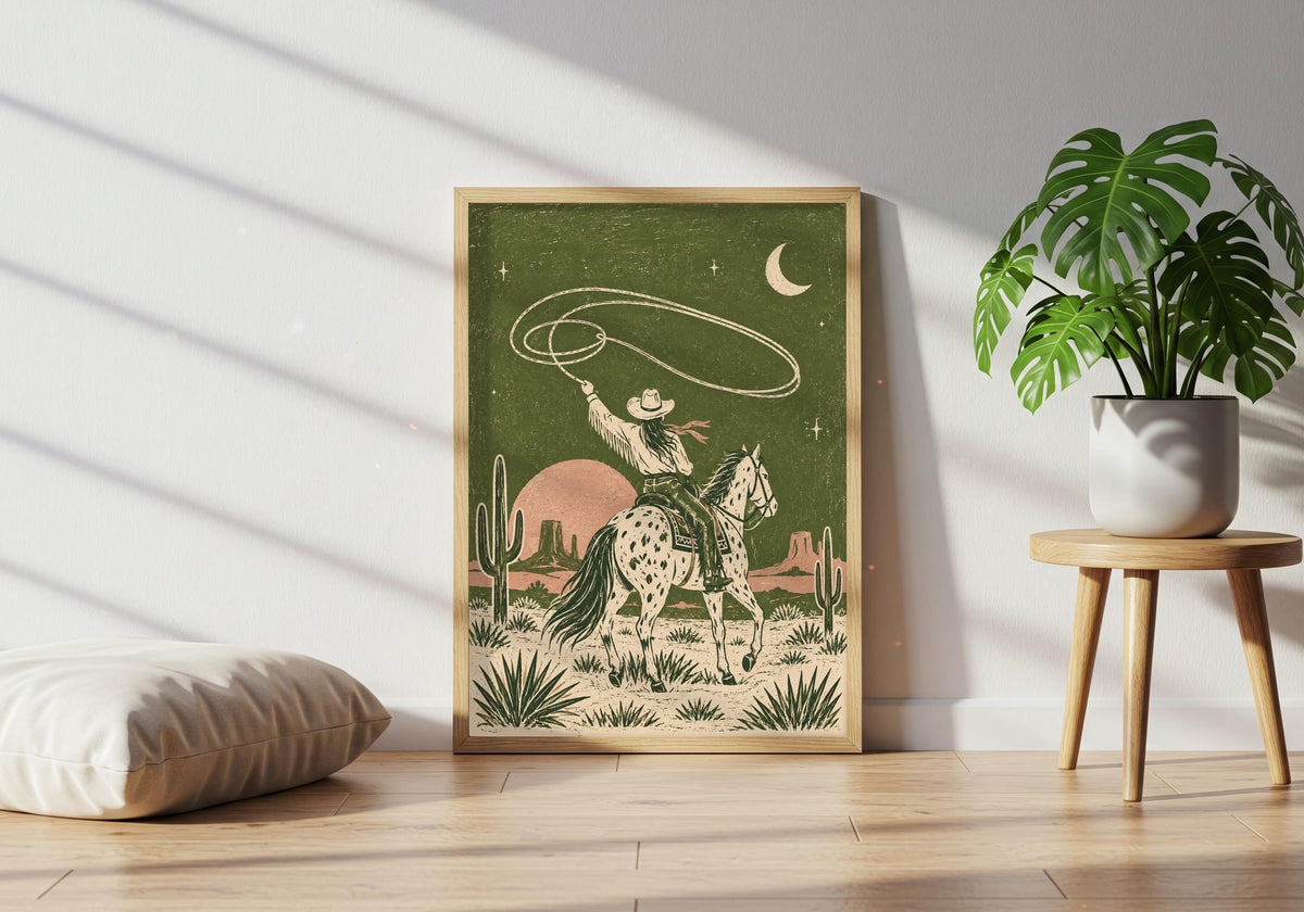 A spotted-horse cowboy twirling a lasso beneath a crescent moon in an olive desert forms the focal point of this horse rider art display in a plant-filled lounge.