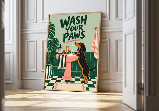 Wash Your Paws wash your paws in a light wood frame, featuring the words Wash Your Paws above a dog standing at a pink sink in a leafy green bathroom.