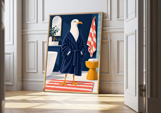 Hotel Bathrobe Seagull seagull bathroom art in a light natural-wood hero frame, featuring a white seagull standing in a hotel bathroom wearing a navy bathrobe beside striped towels, a mirror and yellow stool.