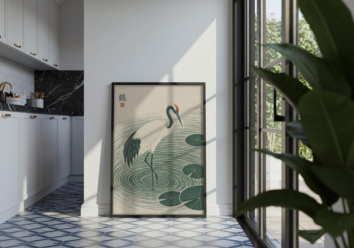 Portrait wabi sabi print featuring a white crane stepping through deep green ripples and lily pads, displayed in a black frame in a tiled interior.