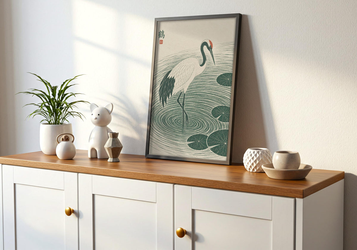 Interior mockup of lily pond poster depicting a white crane stepping through deep green ripples and lily pads, displayed in a black frame on a wooden console.