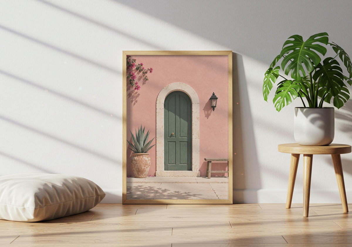 Architecture poster featuring an arched green door in a blush-pink wall with bougainvillea and a wooden bench, leaning in a light wood frame near a healthy green plant.