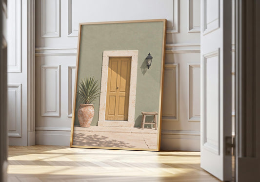 Mustard door print showing a mustard door in a sage wall beside a potted plant, lantern and chair, leaning in a light natural-wood hero frame against white panelling.