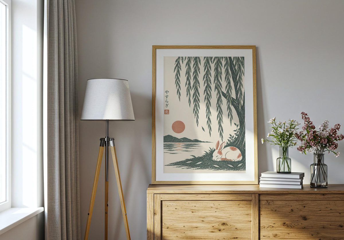 Sleeping Rabbit Under Willow presented as rabbit wall print, featuring a small white rabbit sleeping beside green water beneath long willow leaves and displayed in a light wood frame on a bright console.