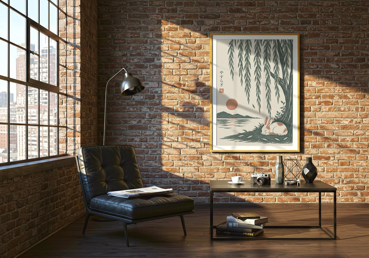Japanese style art with a small white rabbit sleeping beside green water beneath long willow leaves, hung in a pale frame against an exposed-brick wall.