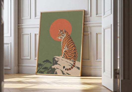Tiger art print showing a striped tiger seated on pale rocks in front of a large red-orange sun, leaning in a light natural-wood hero frame against white panelling.