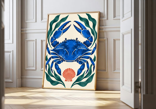 Blue Crab Botanical blue crab wall art in a light wood frame, featuring a vivid blue crab framed by dark green seaweed and a coral shell on cream.