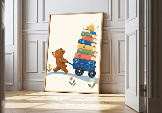 Little Bear's Book Cart bear nursery print in a light wood frame, featuring a small brown bear pushing a blue cart piled high with colourful books.