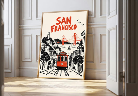 San Francisco Tram san francisco art in a light wood frame, featuring a red cable car travelling through a black-and-white San Francisco street toward the bridge.