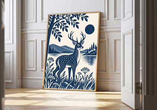 Blue Stag Overlooking the Lake blue stag wall art in a light natural-wood hero frame, featuring a navy stag standing in a flowered lakeside meadow beneath leafy branches, with mountains and a dark blue moon beyond.