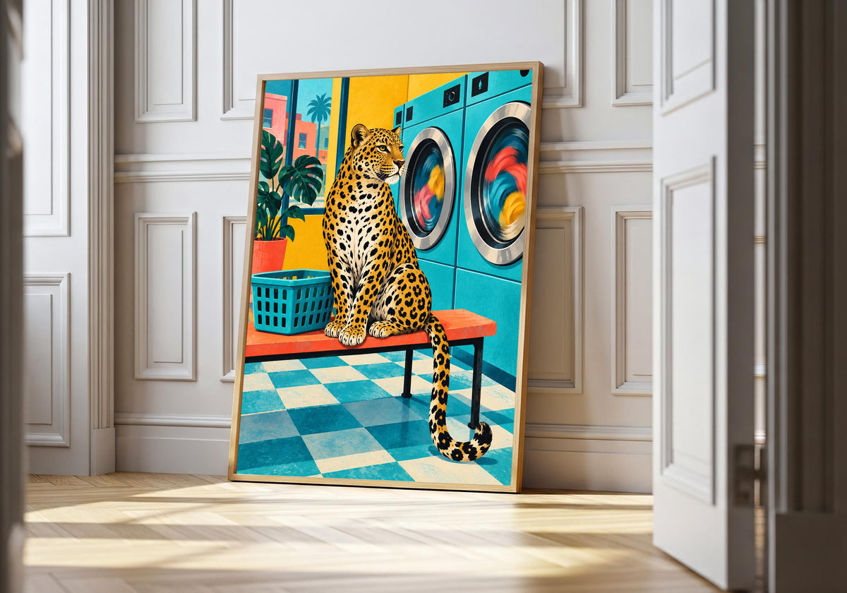 Leopard at the Laundrette leopard wall art in a light natural-wood hero frame, featuring a spotted leopard sitting on a stool in a turquoise retro laundrette beside colourful washing machines and a green laundry basket.