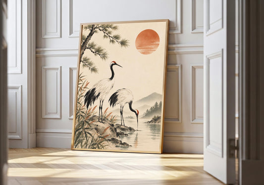 Two cranes and a red sun appear in a nature print leaning in a wood frame against white panelling.
