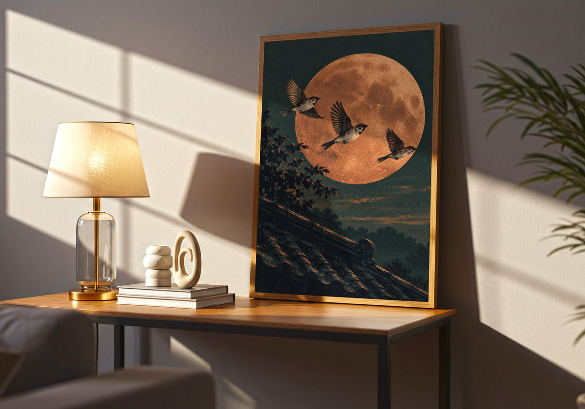 The lamp-lit tabletop view brings attention to a broad moon above the roof in the framed print.