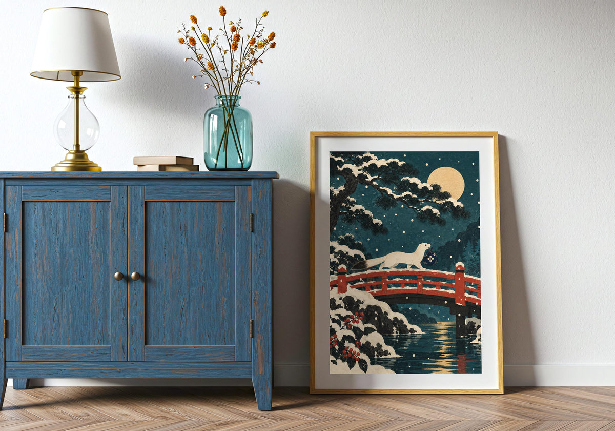 Propped beside a blue cabinet, this framed illustration features the pale moon over the winter scene.